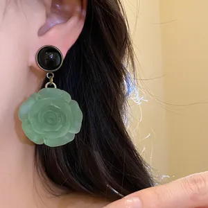 Detail shot of elegant green resin rose dangle earrings with a black stud on model ear