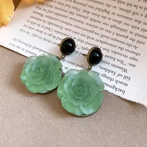Detailed macro view of elegant vintage green resin rose drop earrings with black round studs
