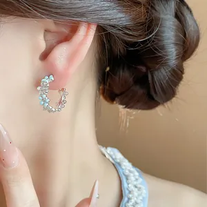 Primo piano di eleganti orecchini a C con delicati fiori in smalto blu e zirconi