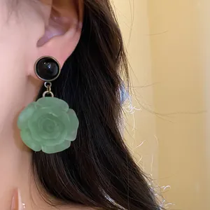 Close-up detail of elegant green resin rose flower drop earring worn on a model's ear