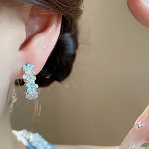 Primo piano di orecchini a C in argento con fiori smaltati blu e zirconi