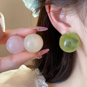 Close-up detail of colorful resin sphere stud earrings worn on ear and held by hand