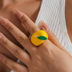Close-up view of a creative yellow apple enamel ring with a green leaf worn on a finger