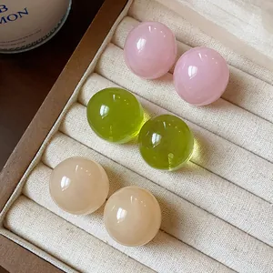 Close-up of glossy round resin stud earrings in pink, green, and peach tones.
