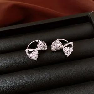 Detailed macro shot of sparkling zircon bow-knot ear cuffs in a black display case.