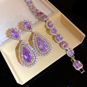 Close-up of sparkling purple teardrop zircon earrings and bracelet set in cream jewelry box