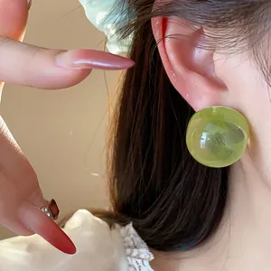 Detail close-up of green resin round stud earrings worn on ear with soft lighting