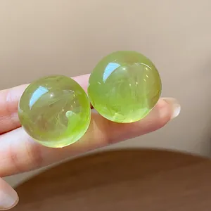 Close-up view of translucent lime green resin ball stud earrings with cloud pattern