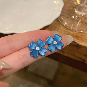 Close-up of blue cat-eye flower earrings with sparkling zircon center on fingers