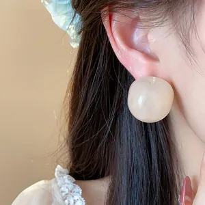 Close-up of large round resin stud earring in cream color worn on ear with dark hair.