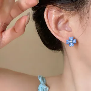 Detail view of a blue flower stud earring with cat's eye stone on model's ear