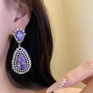 Close-up of elegant purple zircon teardrop hollow pendant earrings on an Asian model's ear.