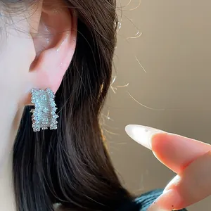 Close-up of elegant silver needle C-shaped earrings with sparkling zirconias on model's ear