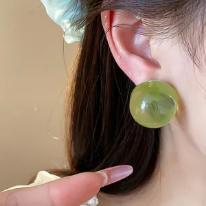Detailed close-up showing a translucent green round resin stud earring on a model's ear.