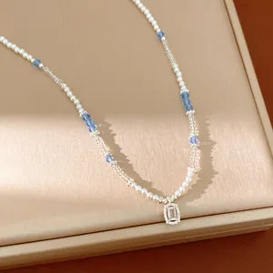 Detailed shot of beaded necklace with pearls, blue crystals and square zircon pendant.