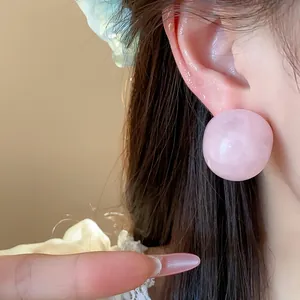 Macro detail of pink resin round stud earrings with marble texture worn on an ear