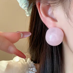 Close-up detail showing a minimalist pink resin round stud earring worn on model ear