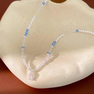 Detailed view of a beaded pearl necklace featuring a square zircon pendant and blue crystals.