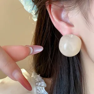 Detailed close-up view showing a minimalist cream round resin stud earring on a person's ear.