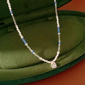 Detailed view of beaded pearl necklace with square zircon pendant and blue crystals.