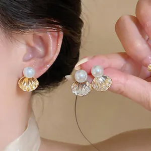 Gros plan sur des boucles d'oreilles élégantes en forme de coquillage doré avec perles.