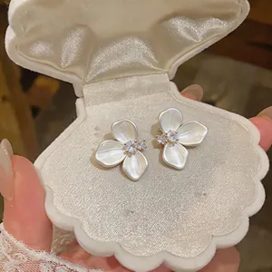 Detail view of elegant camellia flower earrings with sparkling cubic zirconia in a shell box.
