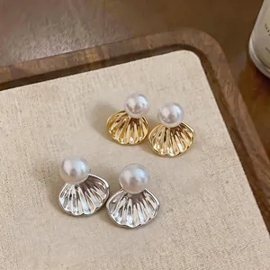 Détail de boucles d'oreilles élégantes en perles et nacre dorées et argentées sur tissu.