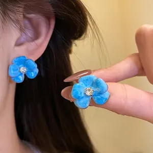Detailed view of blue enamel flower stud earrings with a central crystal on model
