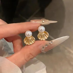 Gros plan de boucles d'oreilles coquillages dorées de style français avec perles fines.