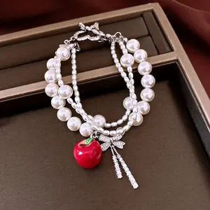 Elegant multi-layer pearl bracelet featuring a zircon bow and vibrant red apple charm