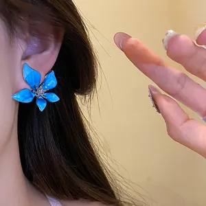 Close-up of blue enamel flower stud earrings with sparkling crystal center on ear