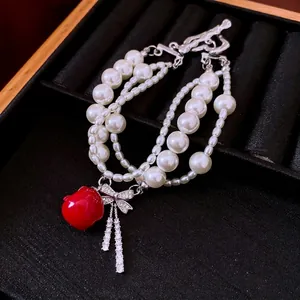 Multi-layer pearl bracelet with zircon bow and red apple pendant on black velvet.