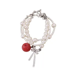 Multi-strand pearl bracelet with red apple charm and zircon bow, minimalist luxury jewelry.
