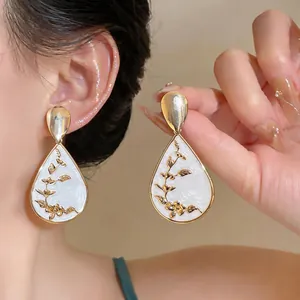 Detailed shot of retro waterdrop earrings featuring golden floral patterns on white enamel