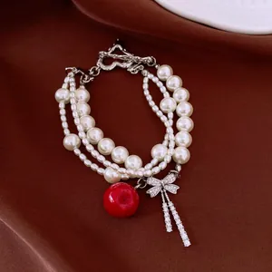 Detail of multi-layer pearl bracelet with red apple charm and sparkling bow tassel.