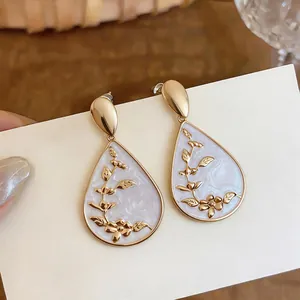 Close-up of elegant gold water drop earrings with white enamel and floral patterns.