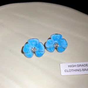Detailed close-up of blue enamel flower stud earrings with a central clear rhinestone