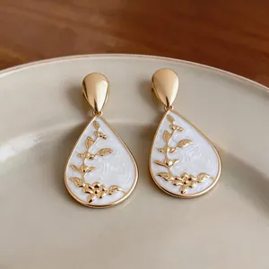 Detailed close-up of elegant teardrop earrings with gold floral patterns on white enamel