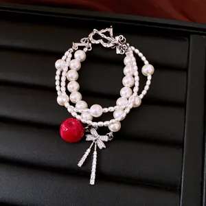 Close-up detail view of elegant multi-strand pearl bracelet featuring red apple and bow