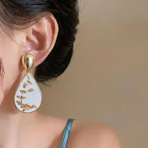 Detailed shot of vintage water drop earrings with elegant gold floral patterns on white enamel