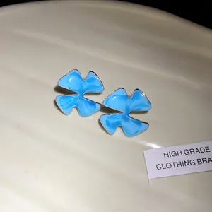 Close-up detail of light blue enamel flower stud earrings with a marbled finish texture