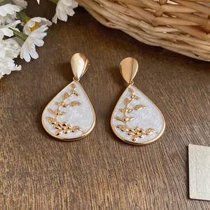Detail of elegant water drop earrings with white enamel and gold floral patterns