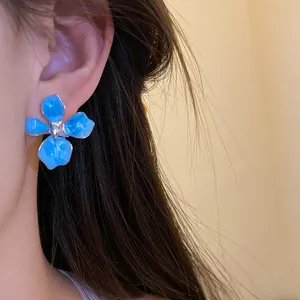 Close-up detail of a blue enamel flower stud earring with a center crystal worn by a model