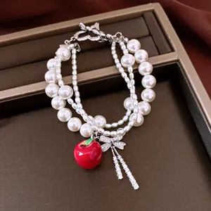 Detailed view of multi-strand pearl bracelet with red apple and crystal bow charms