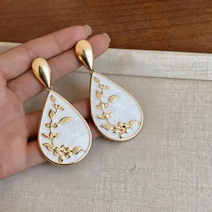 Detailed view of elegant gold floral earrings with white enamel waterdrop design