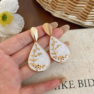 Detailed macro view of vintage white enamel teardrop earrings with gold floral pattern.
