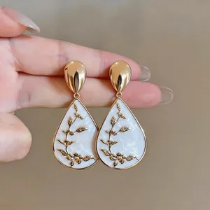 Detailed view of elegant retro gold teardrop earrings featuring white floral enamel design