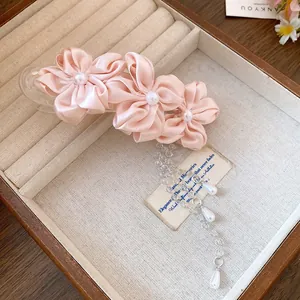 Close-up of elegant pink fabric flower hair clip with pearl tassel in a jewelry box.