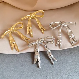 Detailed macro view of golden and silver textured liquid metal bow earrings on fabric
