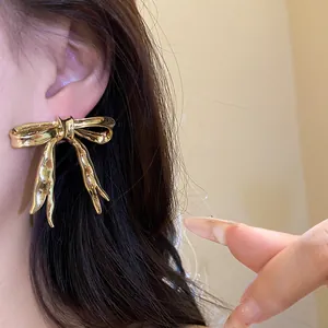 Detailed view of vintage-style gold metallic ribbon bow earrings worn on the ear
